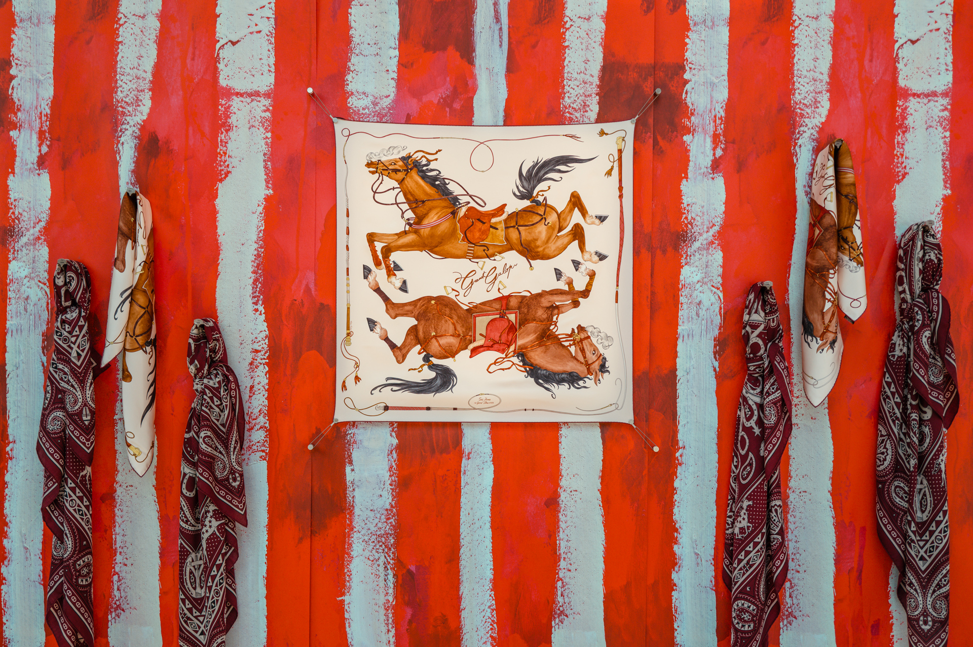 Hermès silk scarves display against a painted backdrop of red and blue stripes