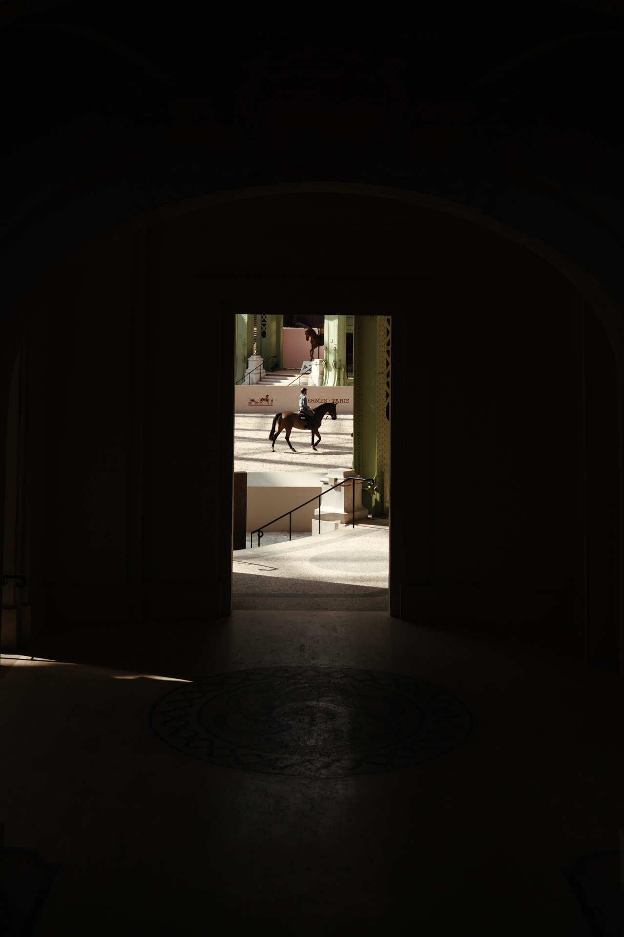 Horse and rider glimpsed through the dark archway entrance of the Grand Palais, silhouetted against the sunlit arena